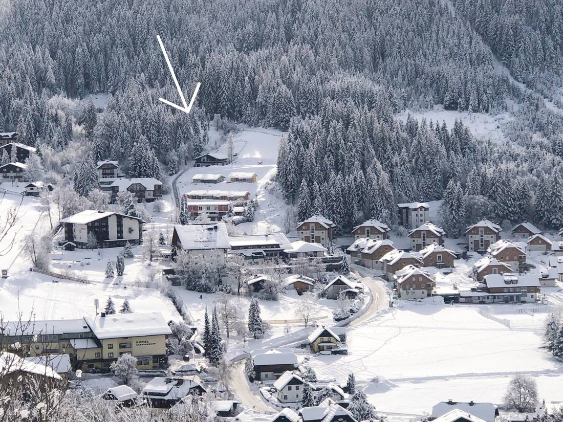 Blick auf das Dorf mit einem Pfeil zur Waldvilla im Wald oberhalb des Ortes